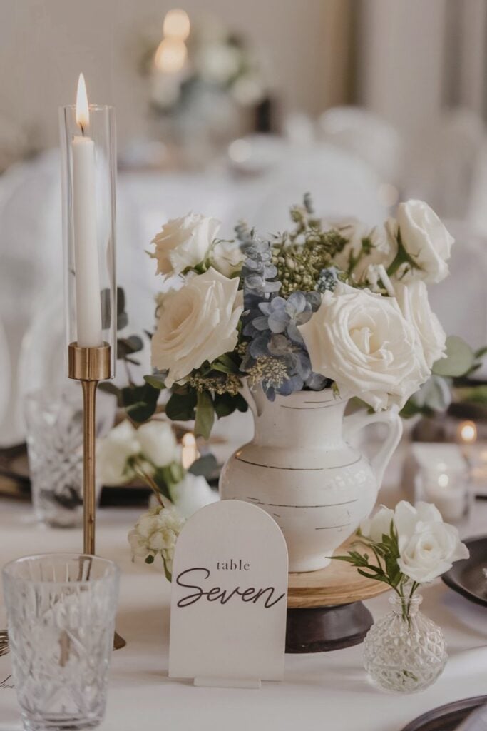 DIY modern wedding centerpiece with white roses and ceramic pitcher.