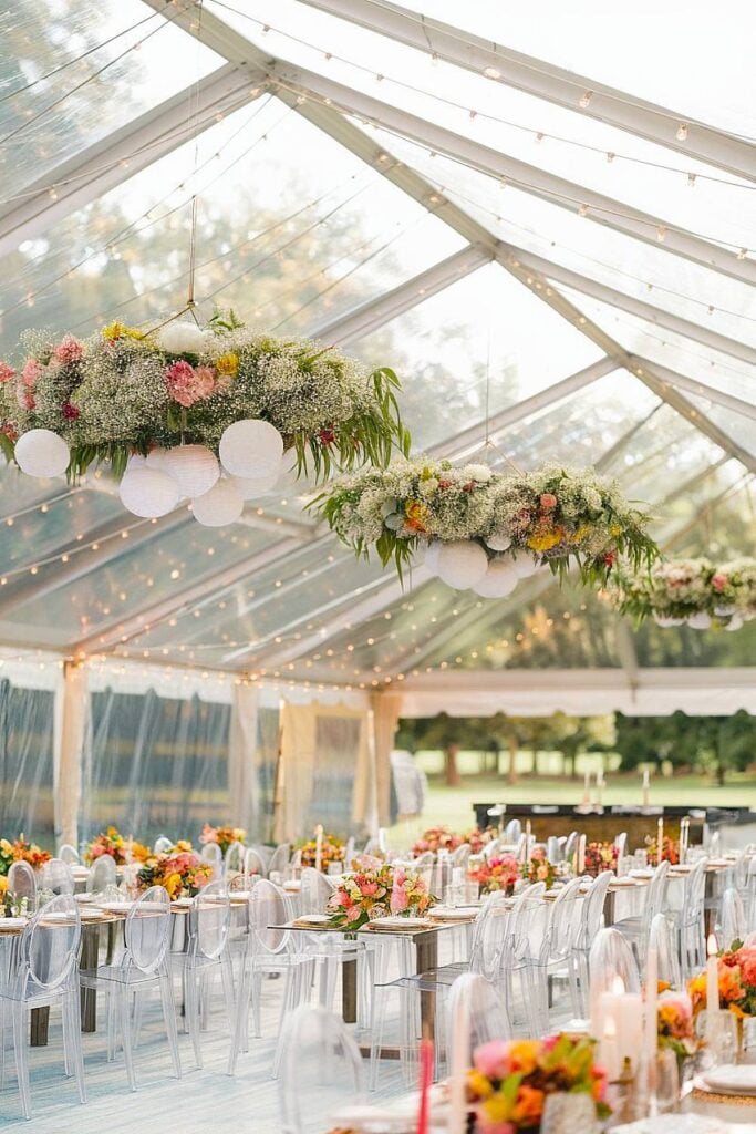 Clear tent with floral chandeliers for backyard wedding reception.