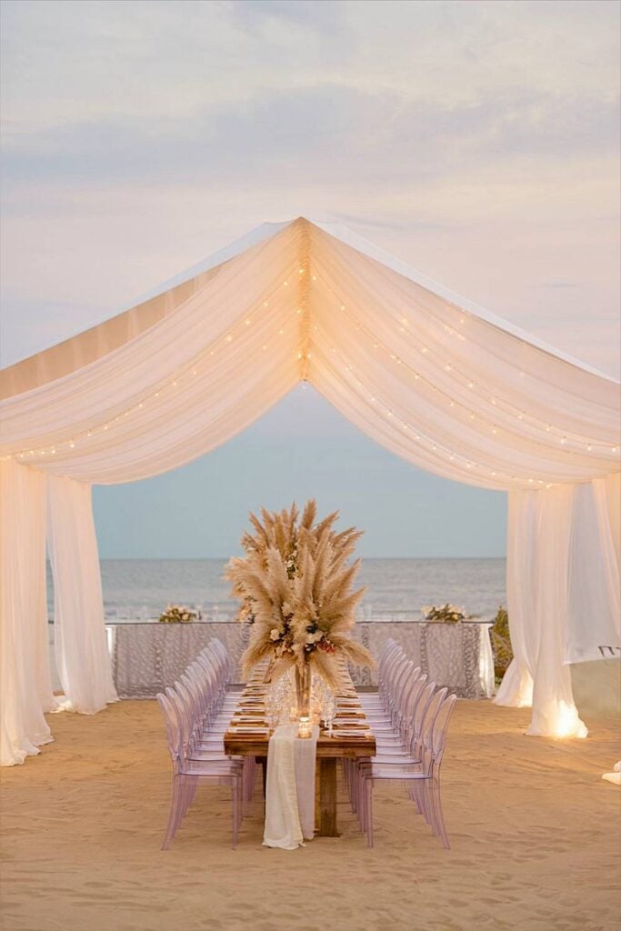 Elegant beach wedding tent with draped fabric and pampas grass centerpiece.