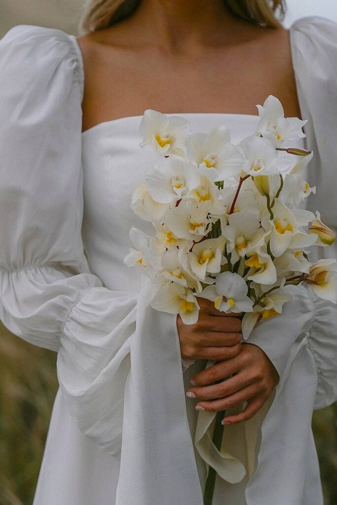 Bride holding white orchid bouquet for backyard wedding.