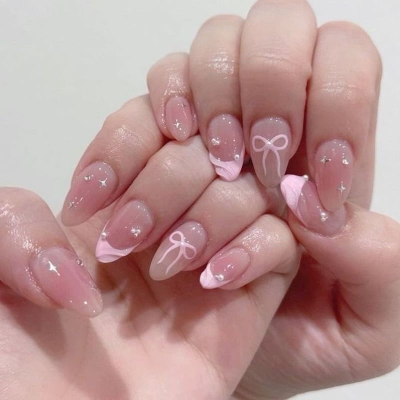 Sheer pink nails with tiny rhinestones and delicate ribbon/bow accents