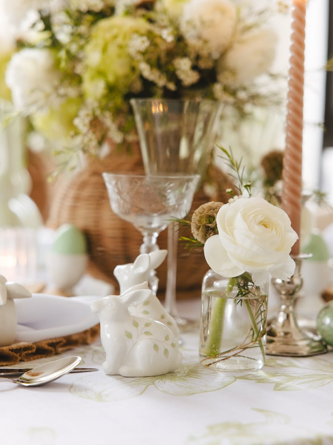 Intimate close-up of a spring table with layered glassware, a small bud vase with a white bloom, cut crystal accents, and soft linen texture in natural light