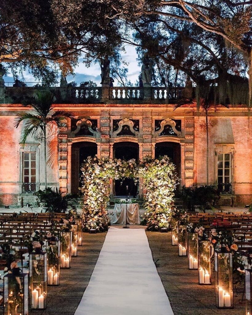 Vizcaya Museum & Gardens wedding ceremony at night with candle lanterns lining the aisle and floral arch — Miami, Florida