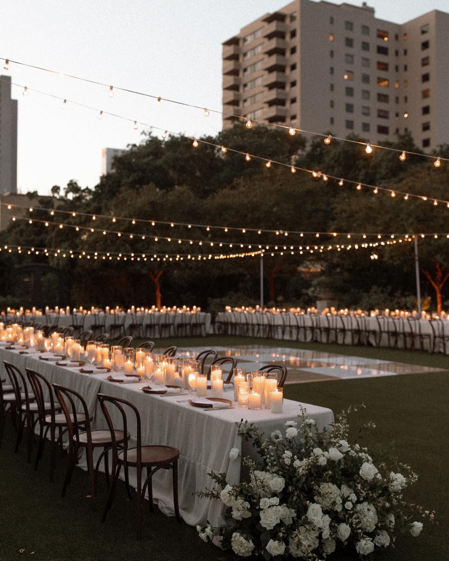360 pillar candles in glass hurricanes ringing outdoor reception with bistro lights overhead
