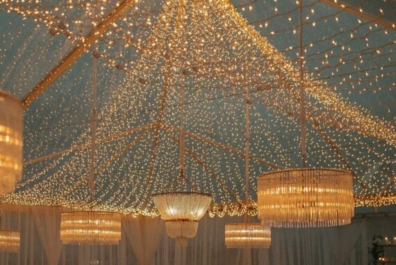 Clear-top tent reception with cascading fairy lights and Edison chandeliers overhead at outdoor evening wedding