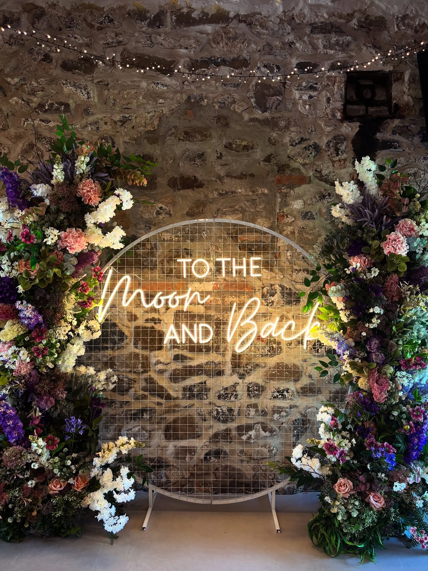 To The Moon And Back custom neon sign with floral arch backdrop at wedding venue
