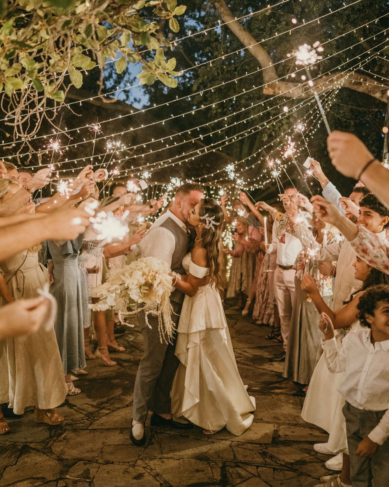 Bride and groom kissing during sparkler send-off under fairy-light canopy of trees