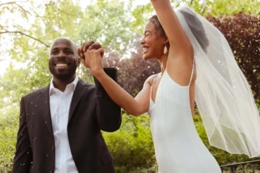 Couple celebrating at their wedding ceremony in a sunny green park, bride in veil and groom in suit