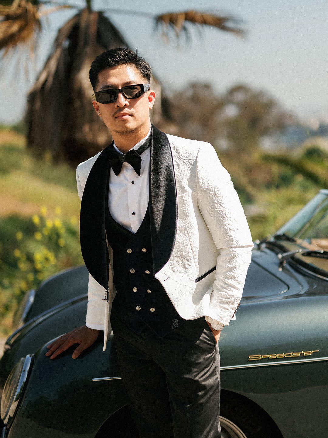 Kevin in a white tuxedo jacket leaning on the Porsche