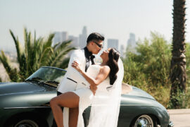 Dyeneka and Kevin kissing by a vintage Porsche with the Los Angeles skyline behind them