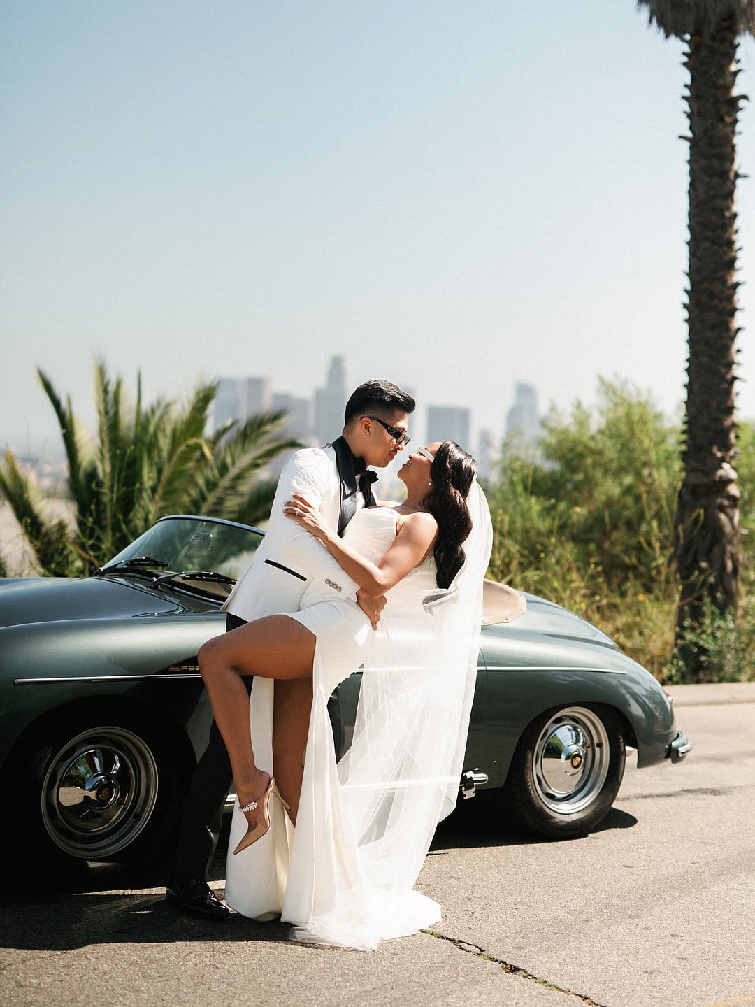 Dyeneka and Kevin kissing by a vintage Porsche with the Los Angeles skyline behind them