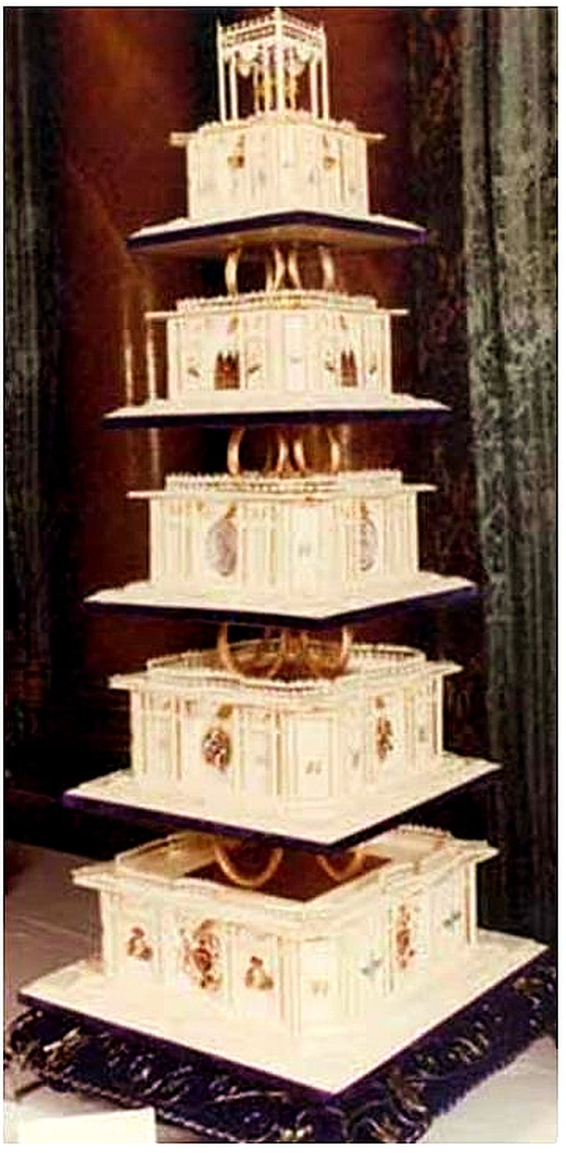 Tall multi-tier square wedding cake made for the 1981 royal wedding of Prince Charles and Lady Diana Spencer, with ornate piped panels and pillars