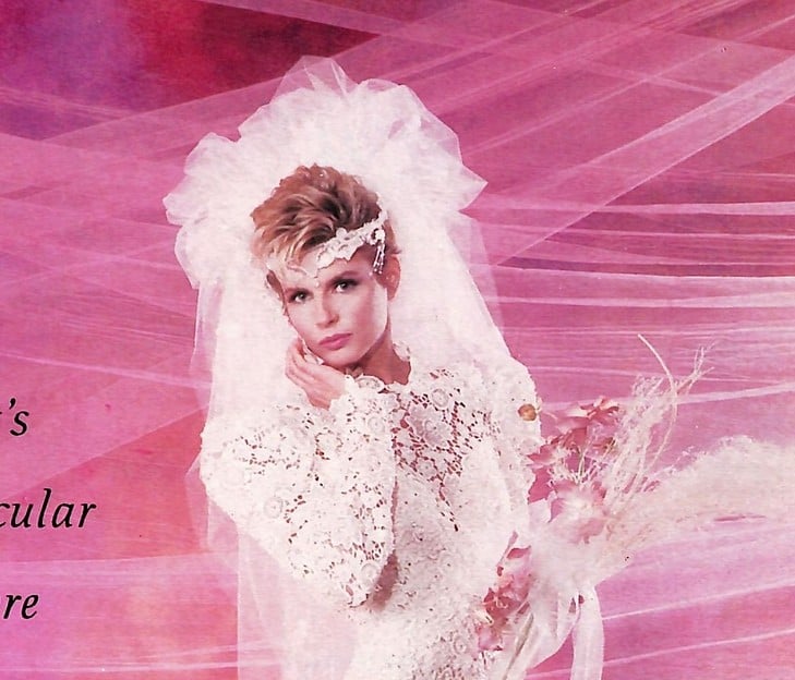 1988 Bellisima ad, bride with short teased crop, lace headband, and enormous tulle pouf veil on a hot pink background