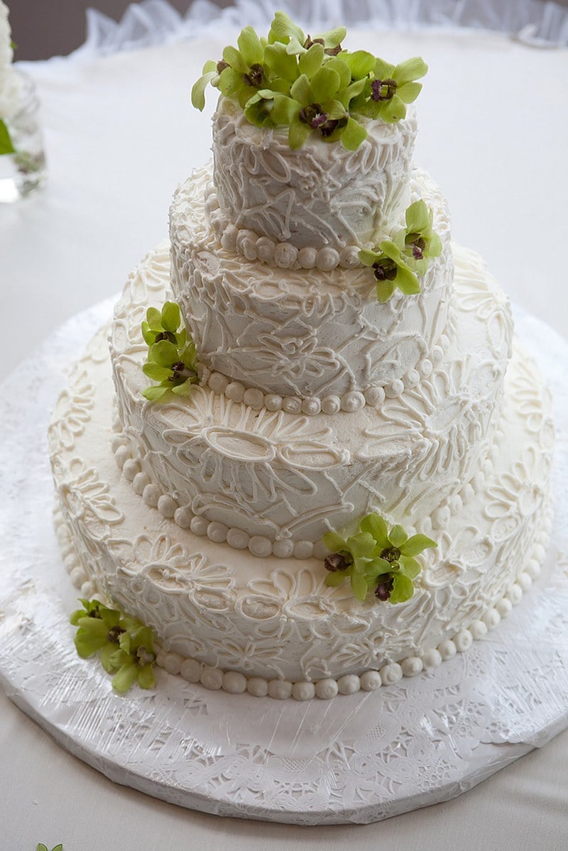 Modern three-tier wedding cake covered in piped buttercream lace with green orchids