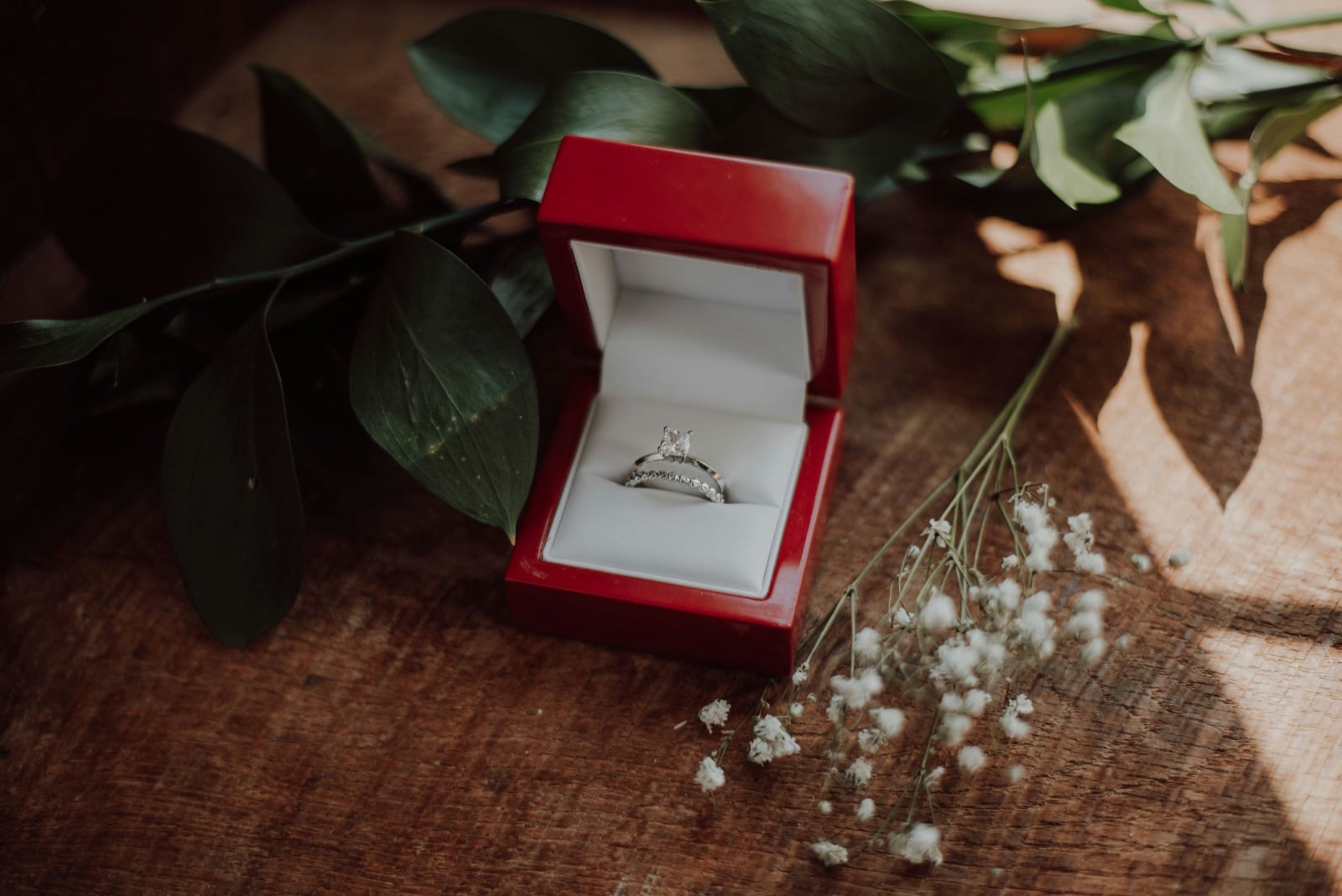 Diamond engagement ring in a red ring box next to baby's breath flowers