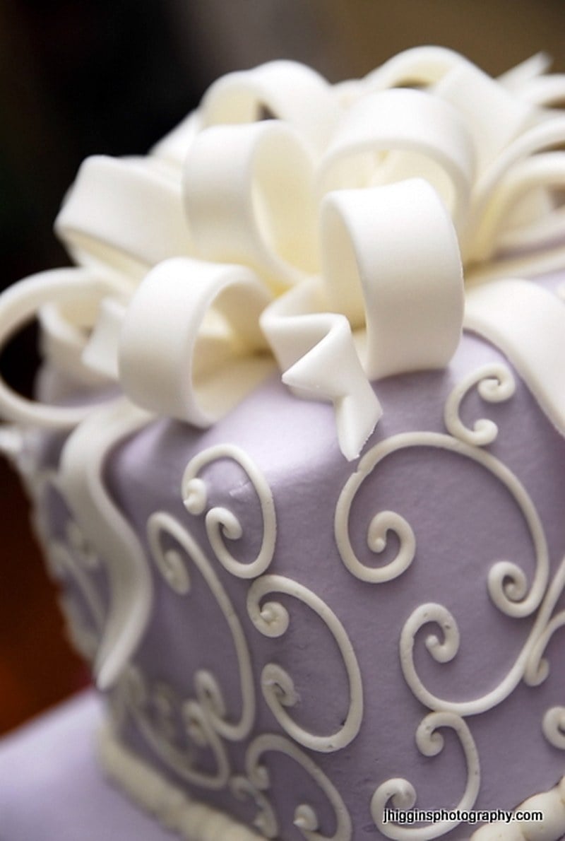 Modern lavender wedding cake with overpiped cream scrollwork and a looped ribbon bow topper in the vintage Lambeth style