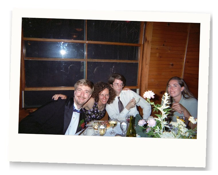 Wedding guests at a 1990s reception table with a single floral centerpiece