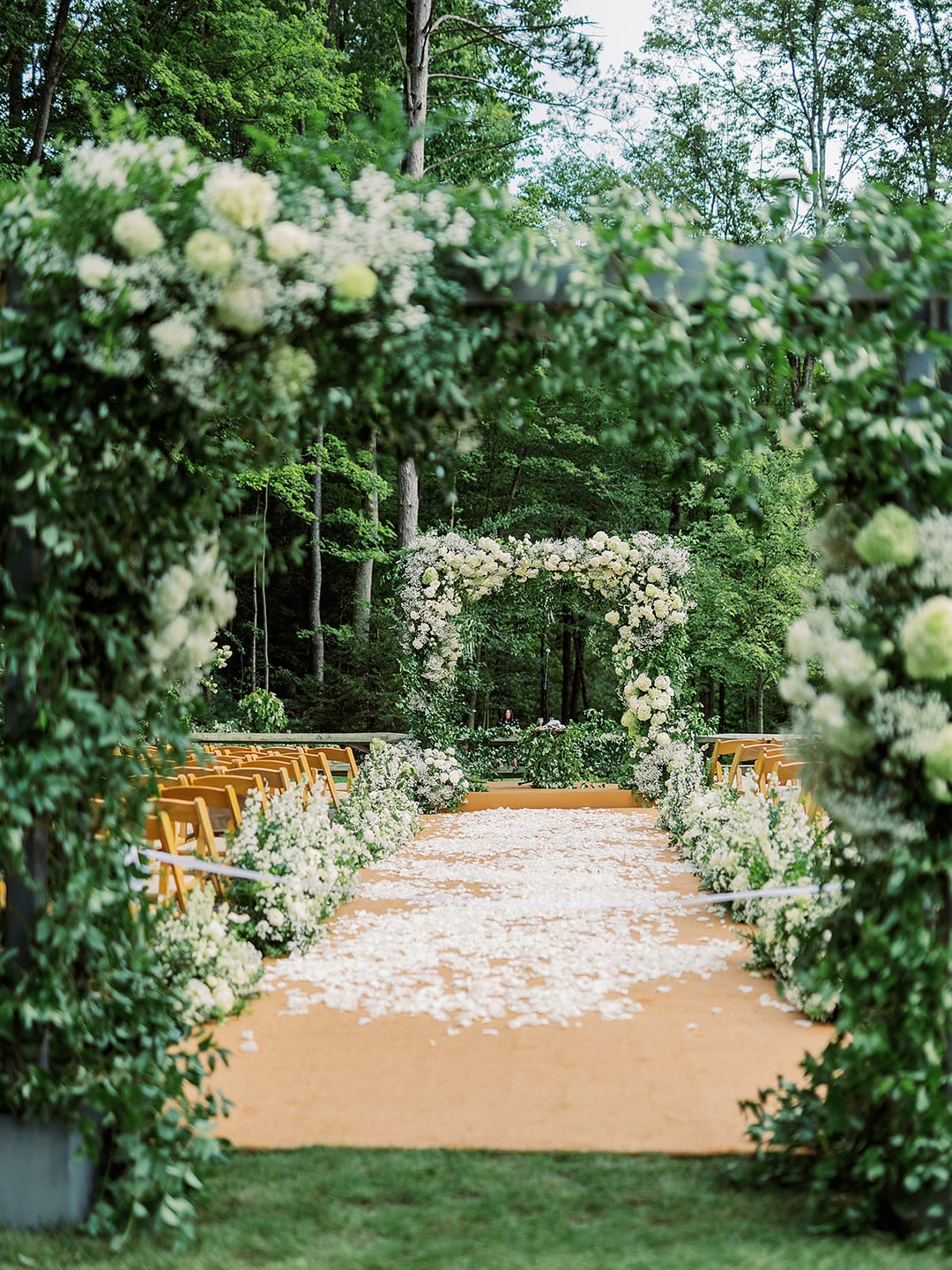 Petal-covered aisle leading to a lush white floral chuppah for a garden ceremony