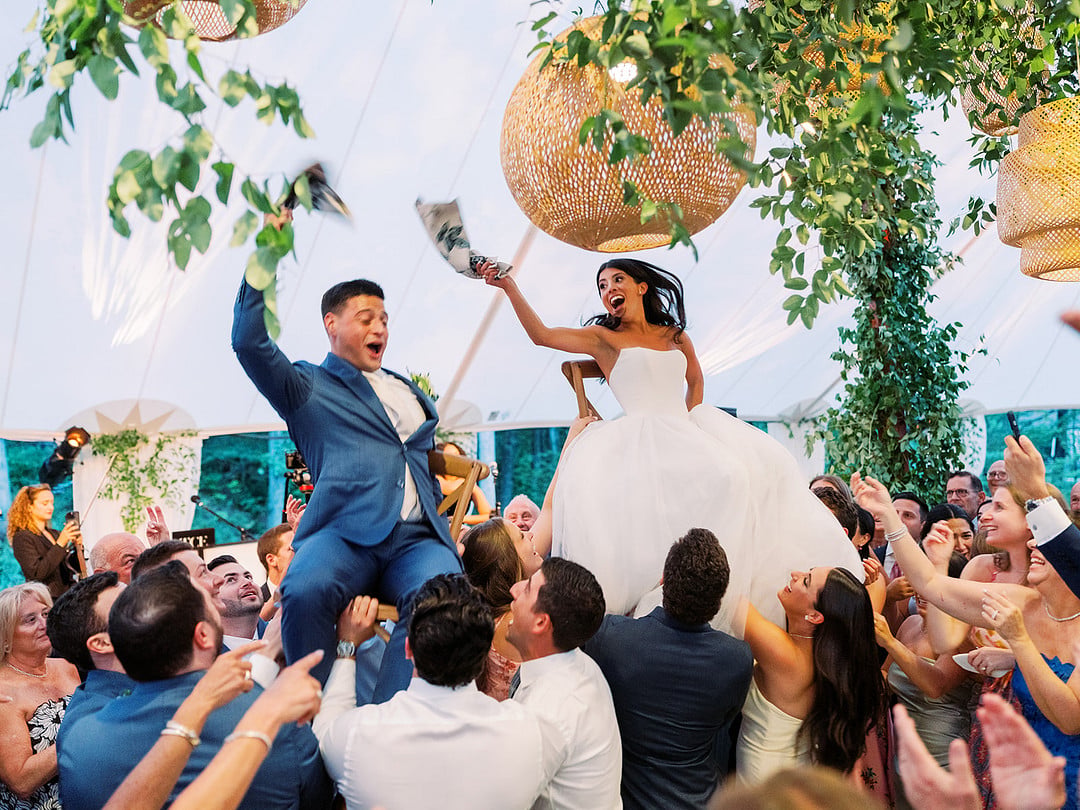 Bride and groom lifted on chairs surrounded by cheering wedding guests