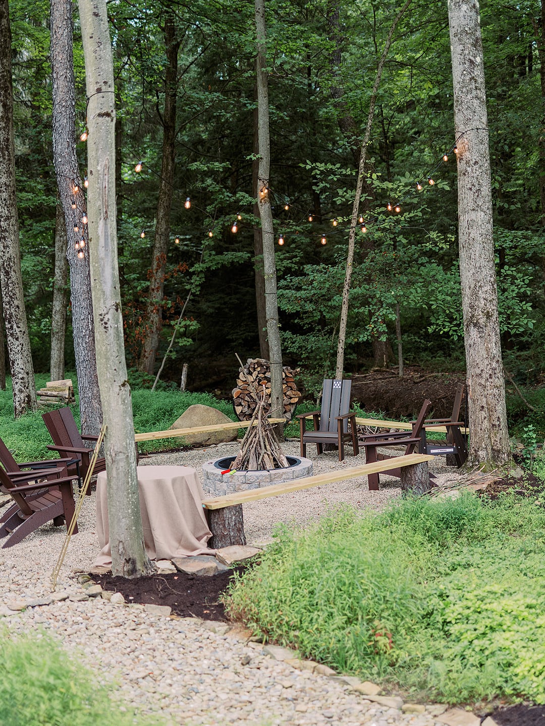 A fire pit and s'mores area tucked into the wooded part of the property with string lights