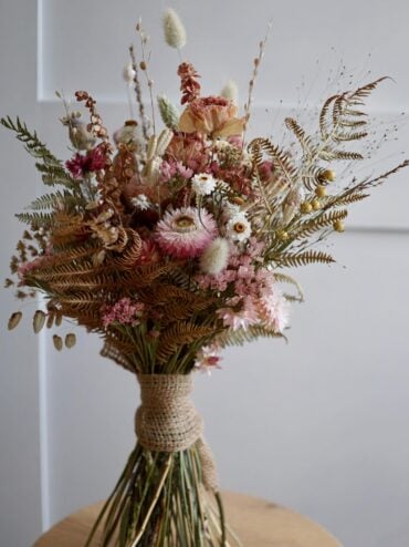 Rustic dried wedding bouquet with strawflowers, statice, bunny tail grass and ferns wrapped in burlap