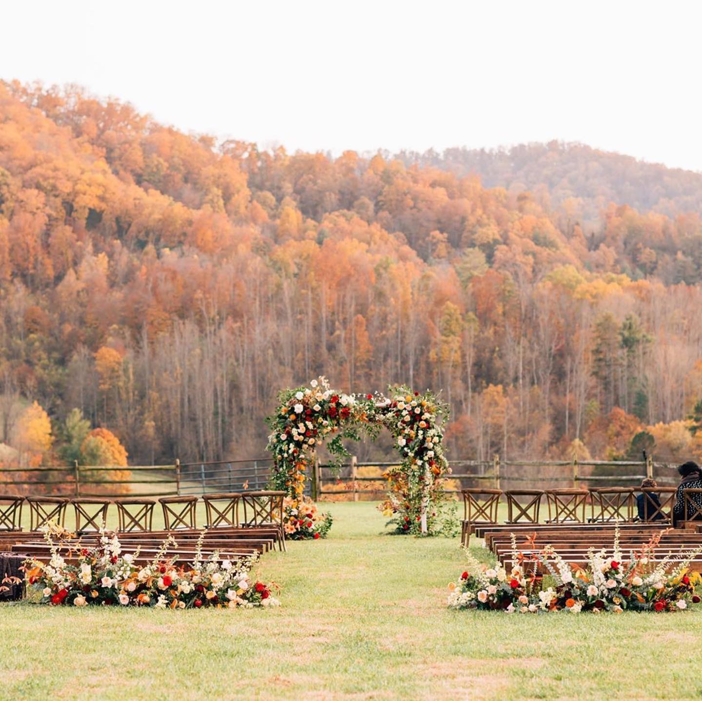 Fall wedding ceremony arch with orange and red flowers and wooden benches in the Blue Ridge Mountains at Claxton Farm