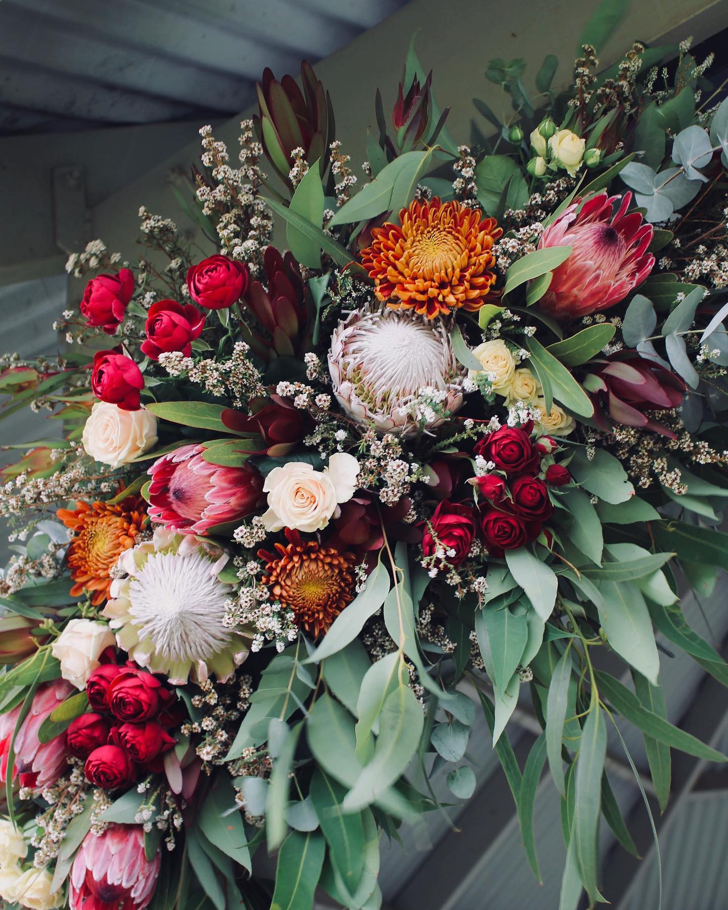 Foam-free rustic wedding arbour arrangement with proteas, roses, baby's breath and eucalyptus