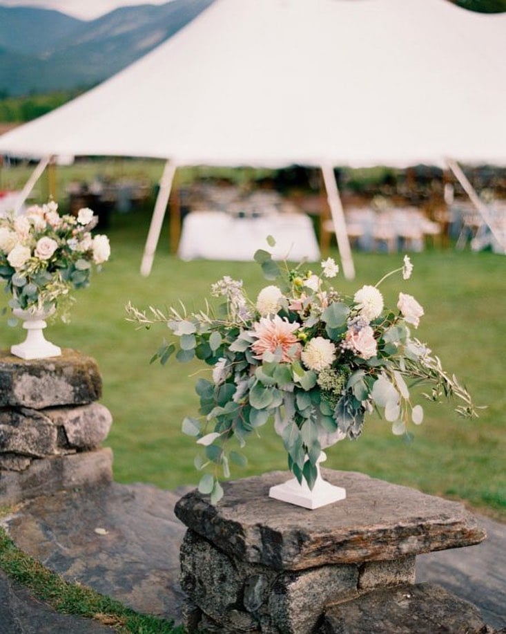 White urns filled with eucalyptus and blush flowers flanking a sailcloth tent entrance at an outdoor wedding