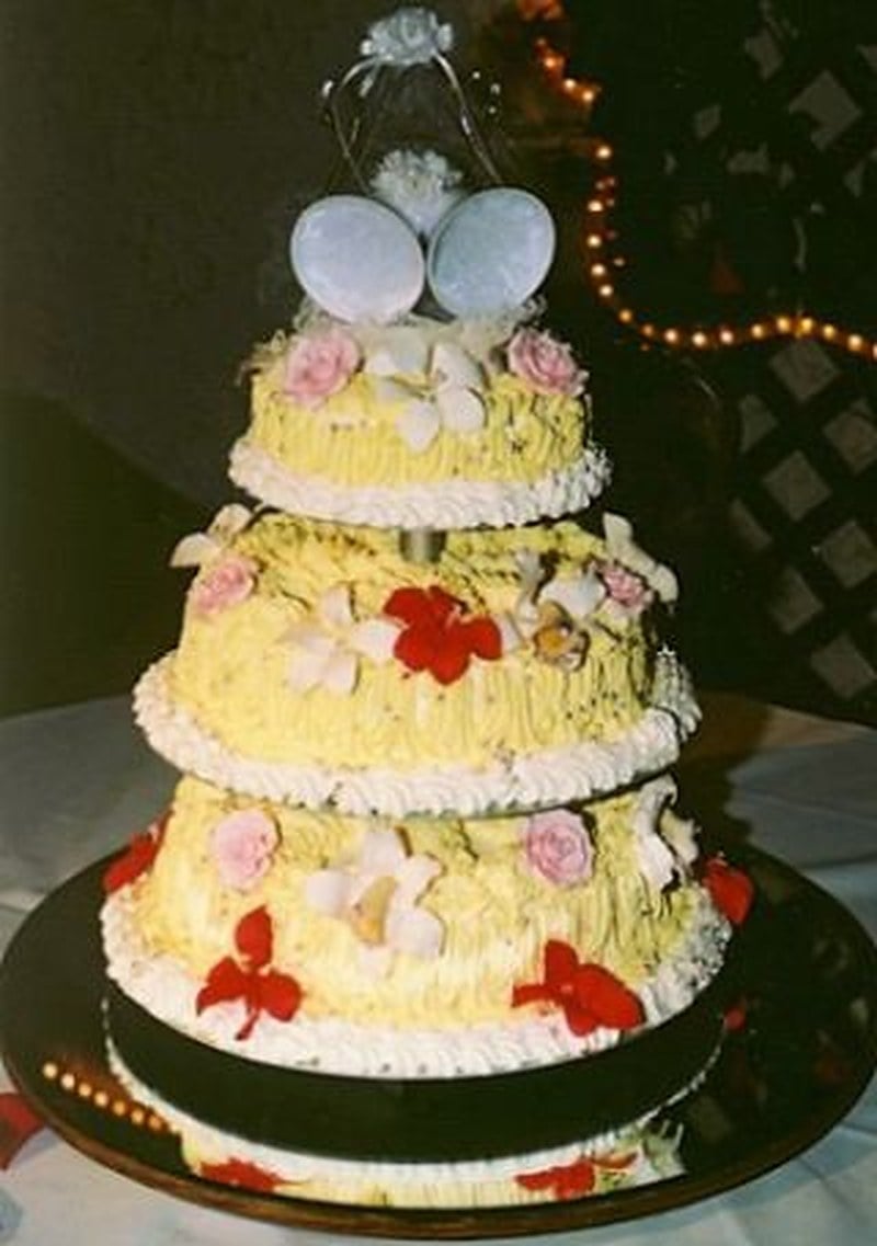 Buttercream wedding cake with textured yellow frosting, small piped flowers, and white wedding bells as the topper