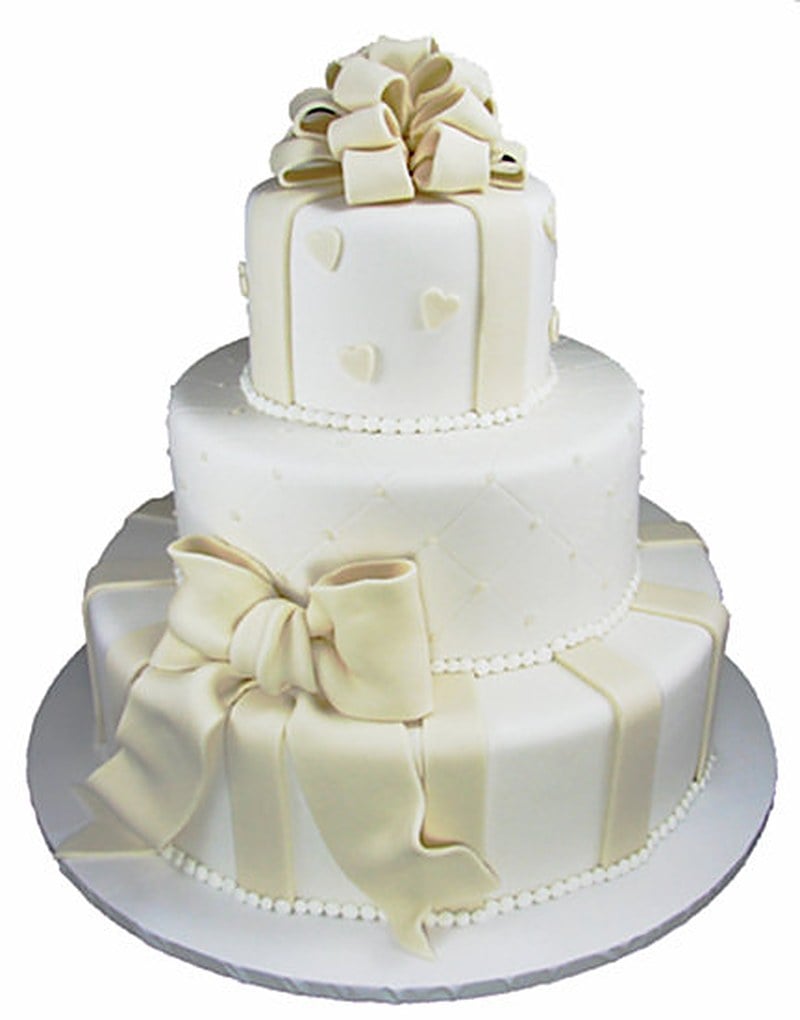 White fondant wedding cake decorated with hearts, bows, and a piped strand of pearls