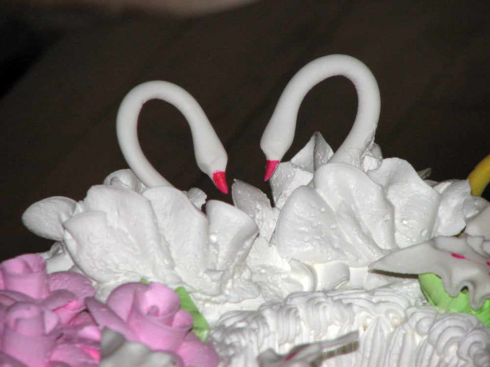 Close-up of two white icing swans with curved necks facing each other on a ruffled wedding cake
