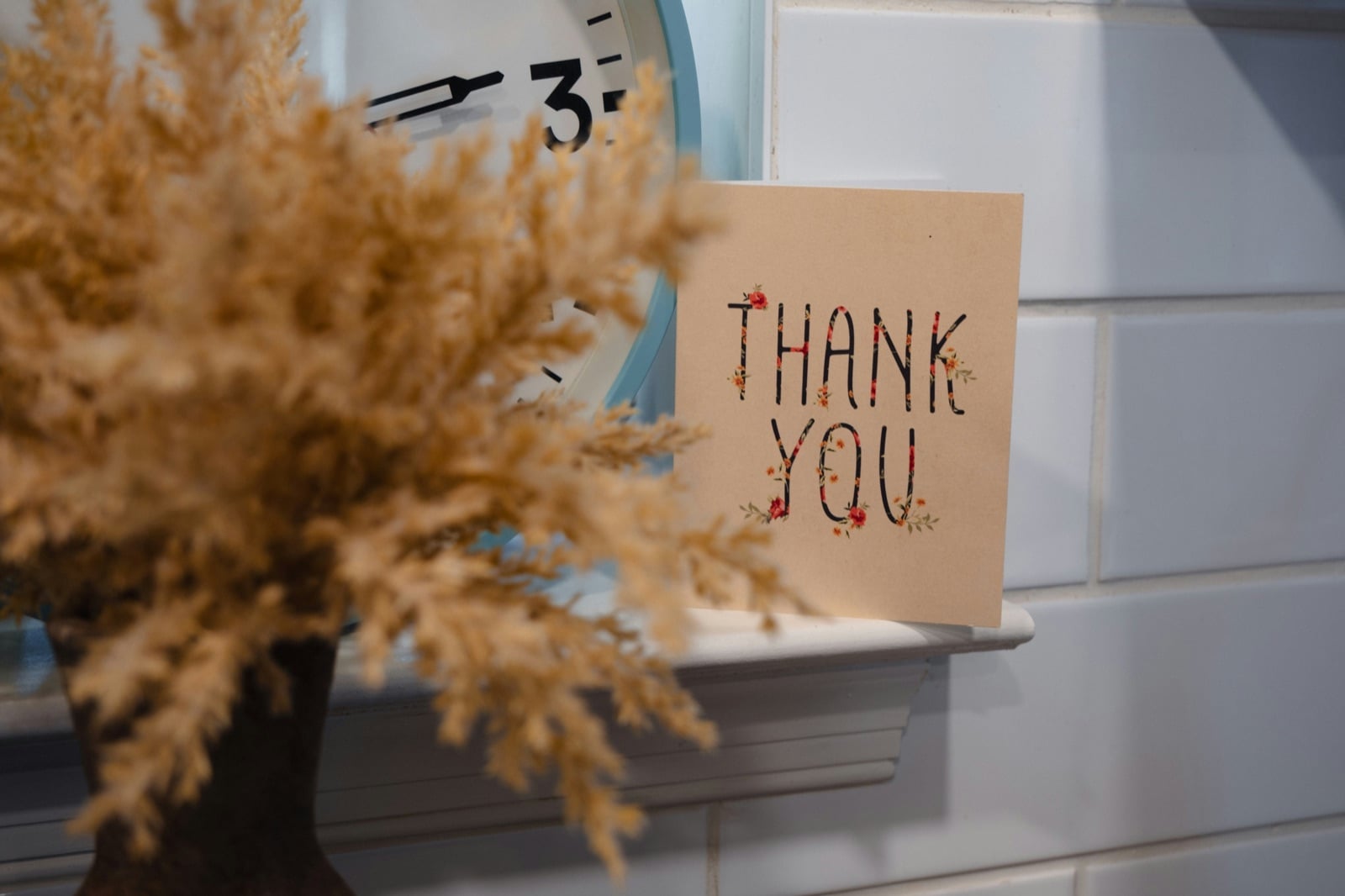 Floral thank you card propped on a shelf next to a clock