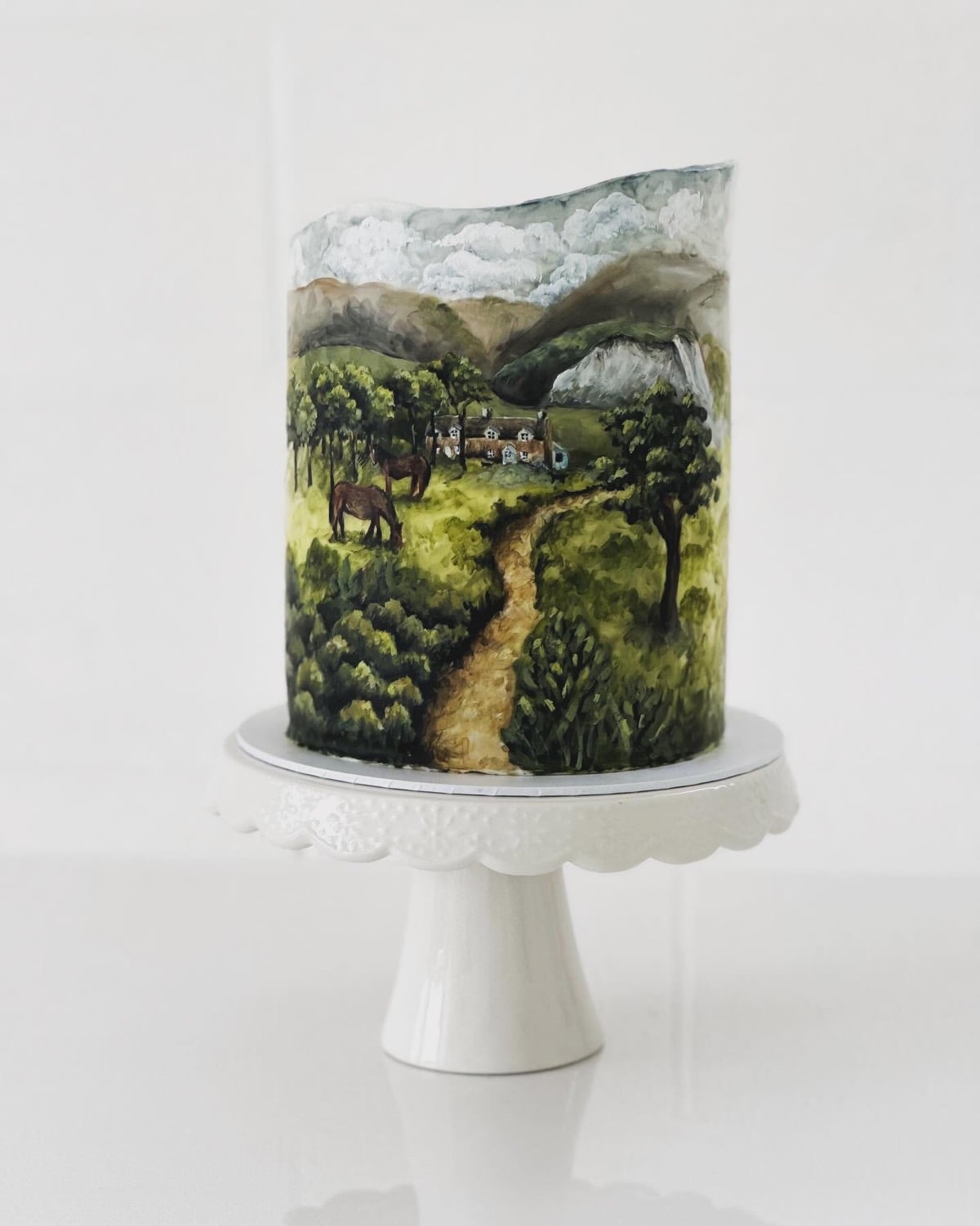 Hand-painted western wedding cake with a countryside scene of a horse, farmhouse, and winding path