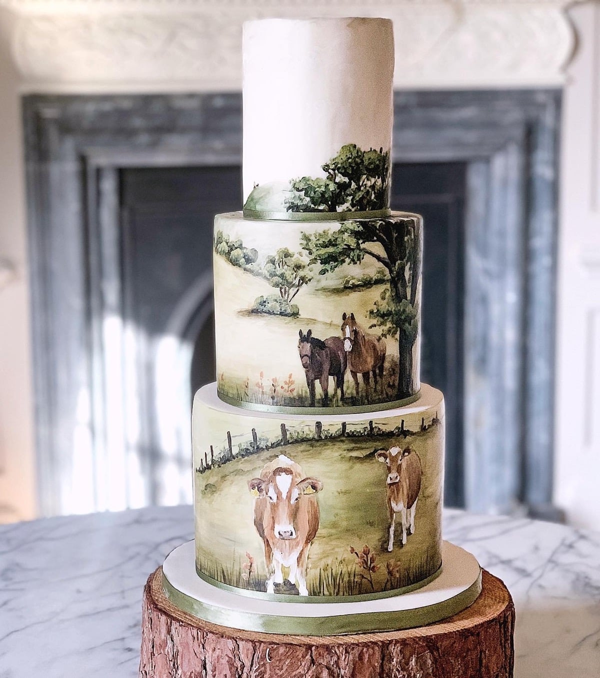 Three-tier wedding cake hand-painted with cows and horses grazing in a pasture
