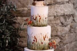 Wedding cake painted with prairie grasses and wildflowers, topped with two cuddling foxes