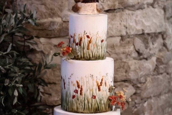 Wedding cake painted with prairie grasses and wildflowers, topped with two cuddling foxes