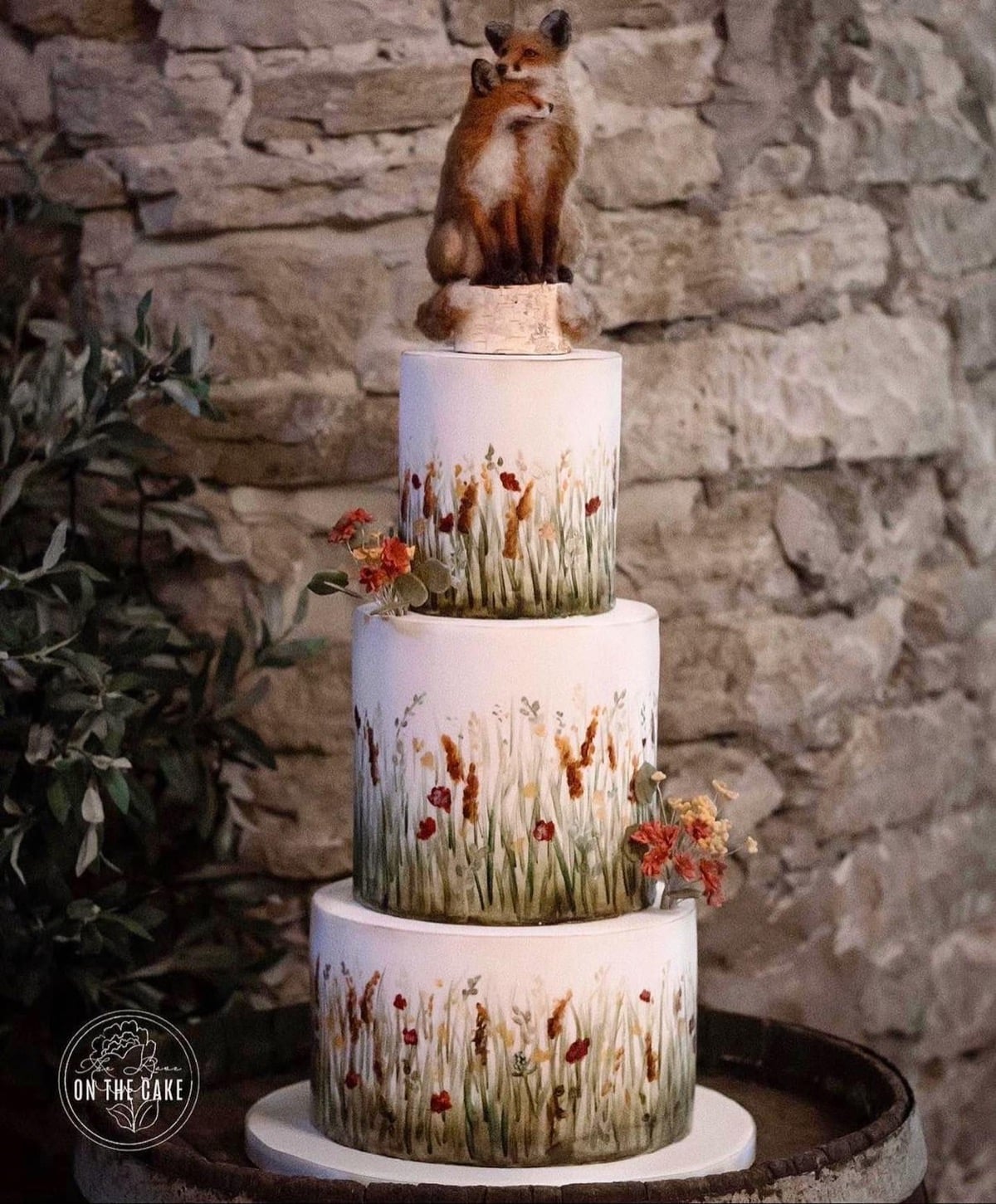 Wedding cake painted with prairie grasses and wildflowers, topped with two cuddling foxes