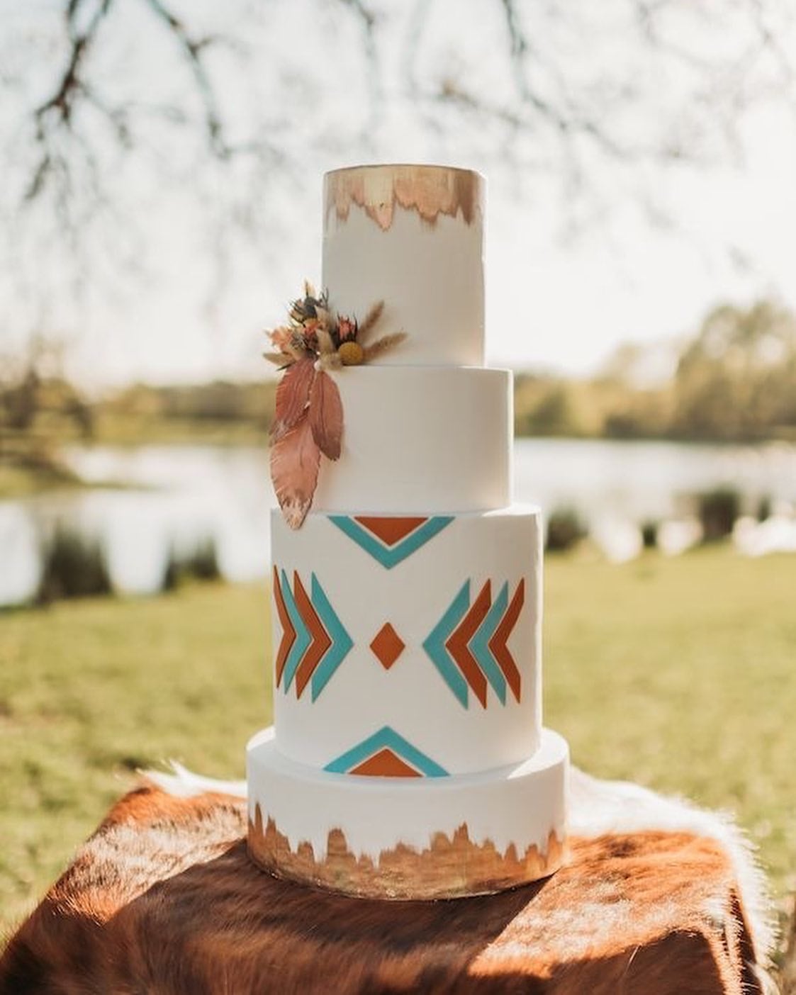 Western wedding cake with turquoise and rust southwestern arrows and gold leaf, displayed on a cowhide