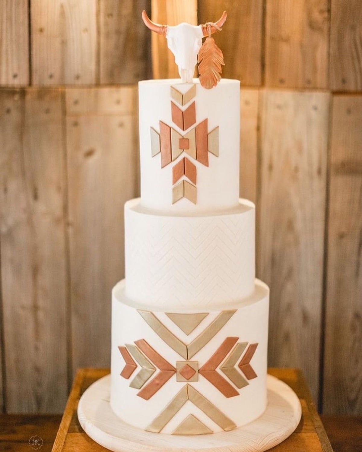 Wedding cake with a white cow skull topper, copper feather, and southwestern tile patterns