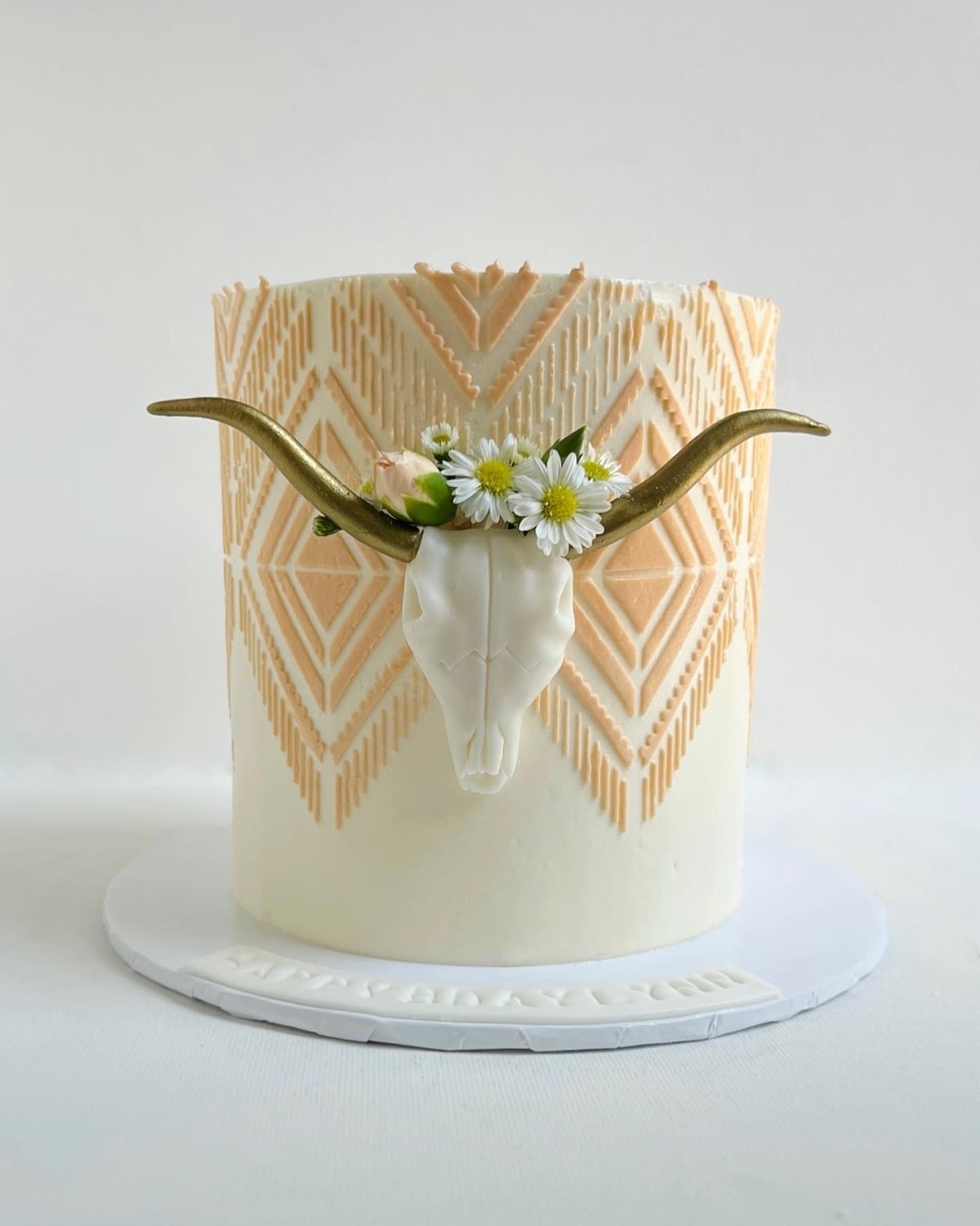 Wedding cake with a gold longhorn skull wearing a daisy crown over a peach southwestern stencil pattern