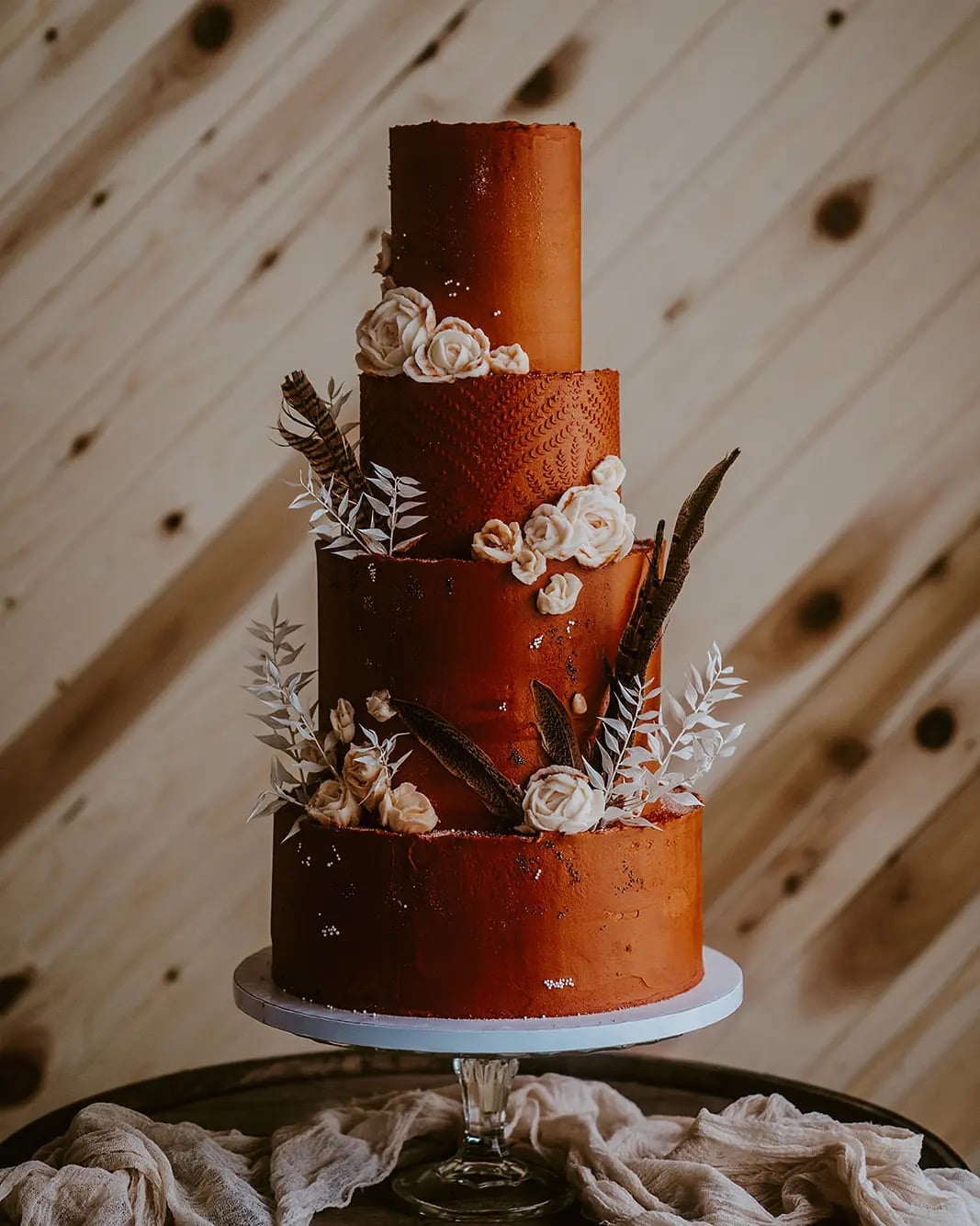 Four-tier burnt orange wedding cake with cream sugar roses and dark feathers