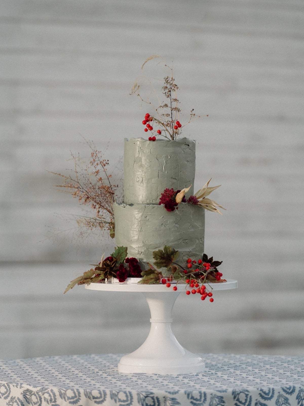 Rustic sage green buttercream wedding cake with red berries and dried stems