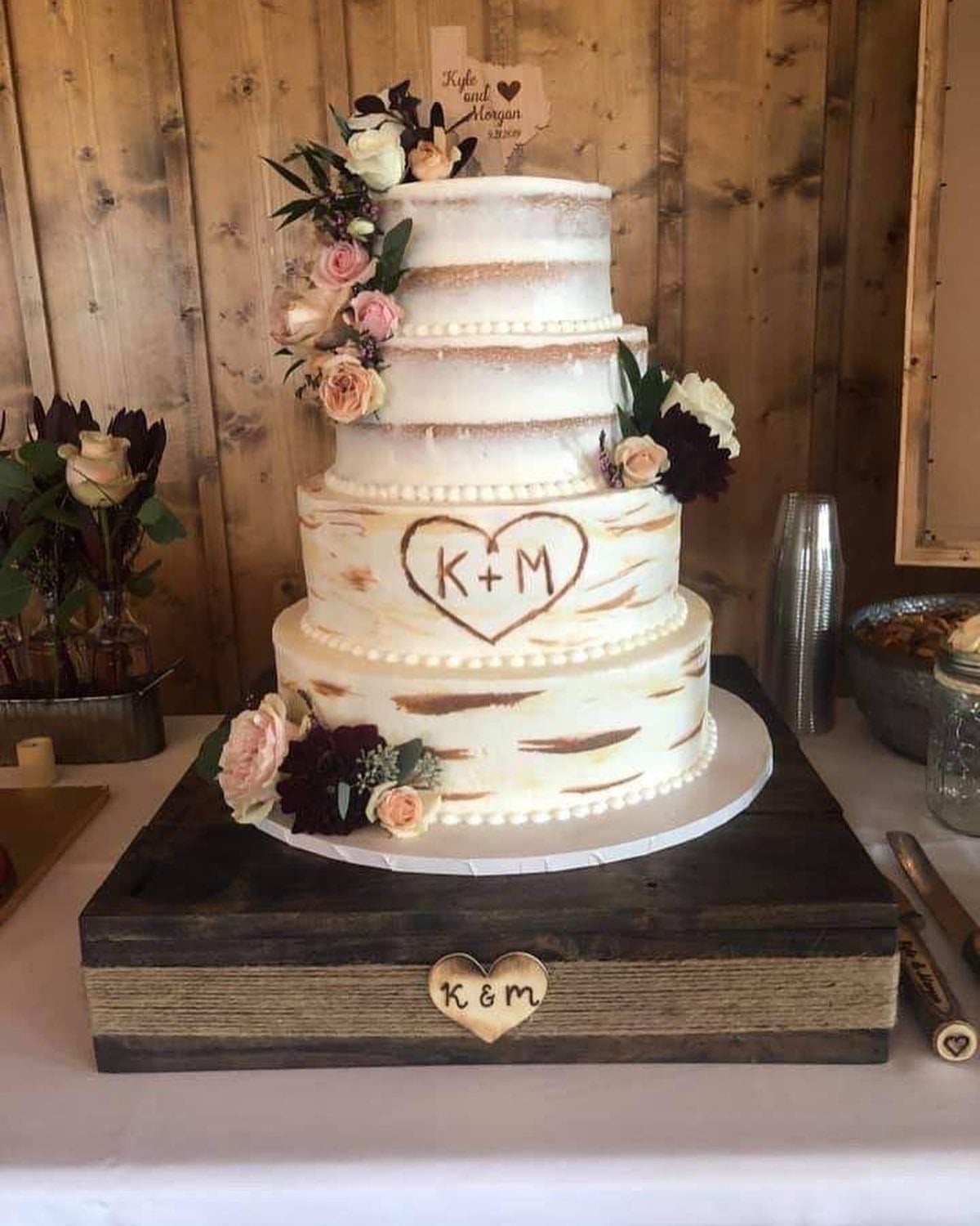 Birch bark wedding cake with the couple's initials carved in a heart, displayed on a wood stand