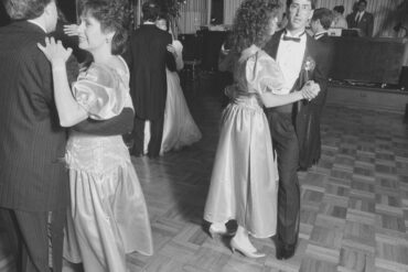 Wedding guests dancing at a 1989 reception, big permed hair and puffed satin sleeves, the bride dancing in the background