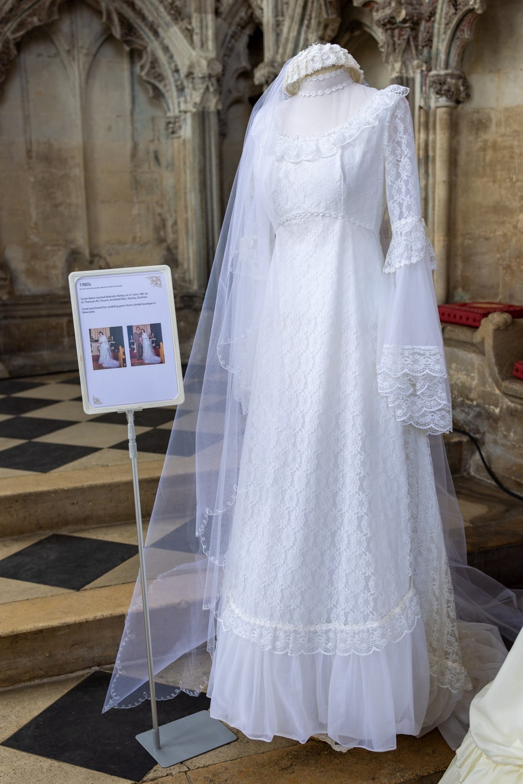 1981 wedding dress on a mannequin with a high Victorian neckline, long fitted lace sleeves, and a lace-trimmed skirt at the Ely Cathedral bridal gown exhibition