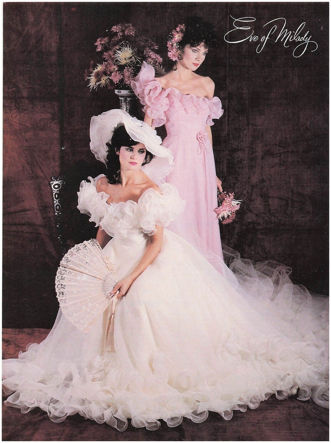 1983 Eve of Milady bridal advertisement: bride in an off-the-shoulder ruffled organza wedding dress with a wide-brim hat and lace fan, attendant in pink behind her