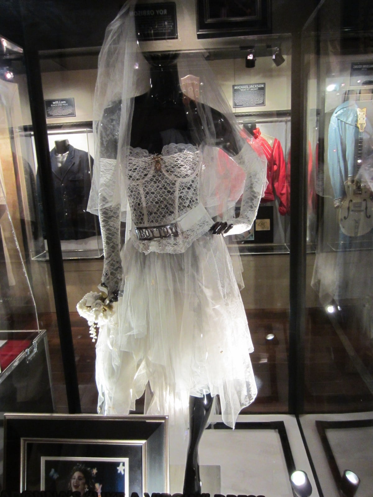 Madonna's 1984 'Like a Virgin' wedding dress with a lace bustier, tulle skirt, veil, and 'Boy Toy' belt in a display case at a Hard Rock Cafe exhibition