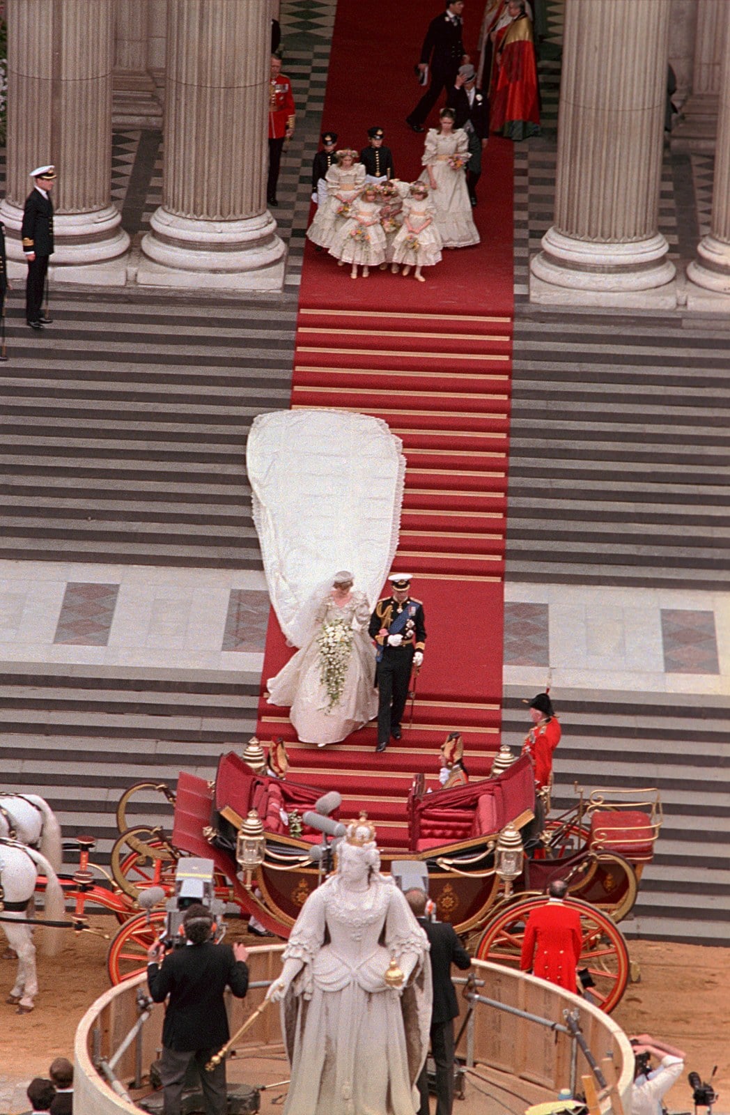 Prince Charles and Princess Diana on the red-carpeted steps of St. Paul's Cathedral on July 29, 1981, with the wedding dress train spread down the stairs and the carriage waiting below