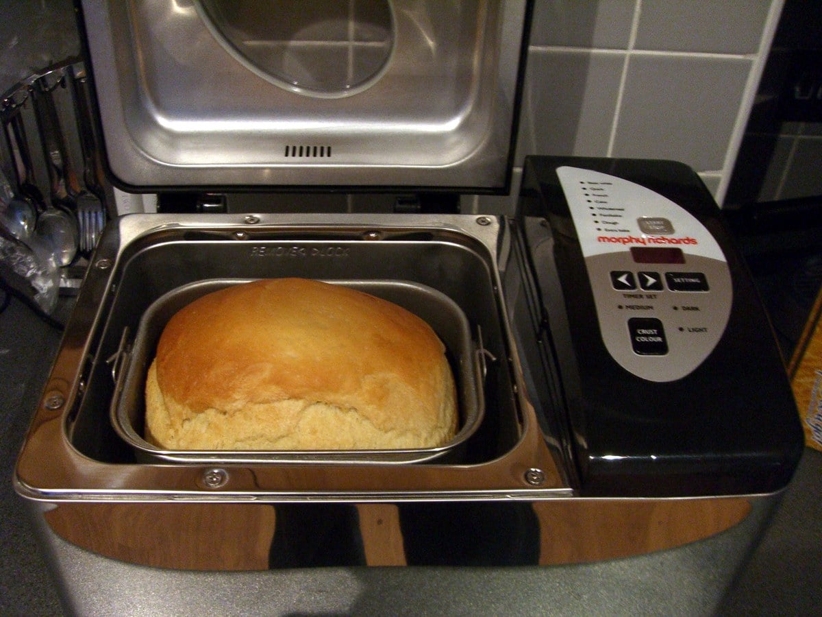 A bread machine with the lid open showing a finished golden loaf