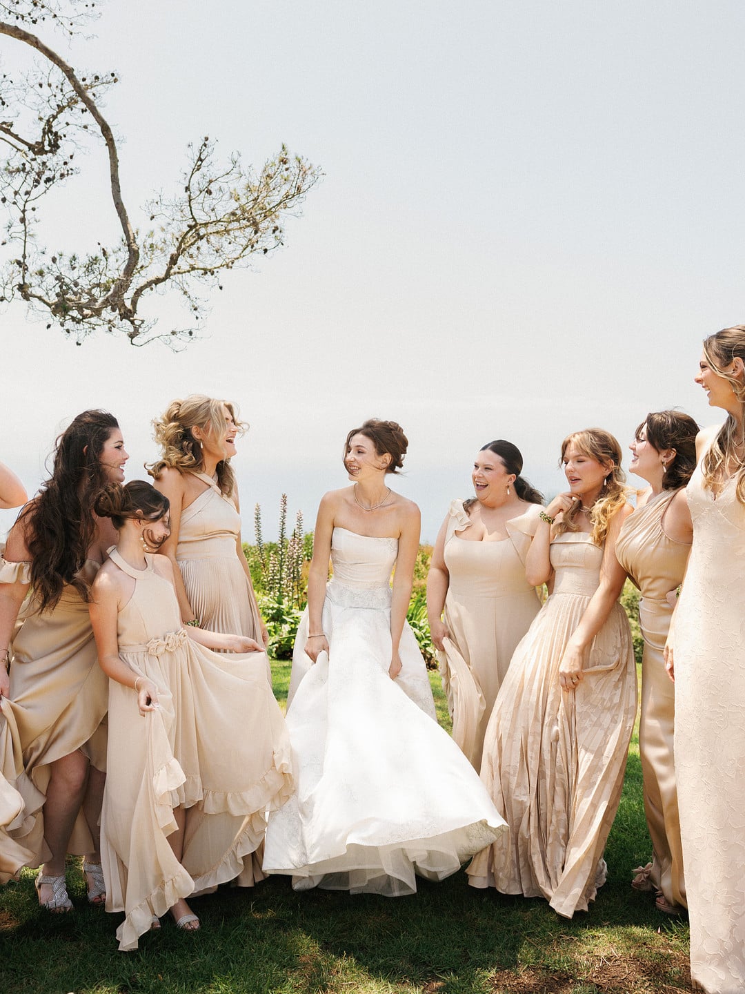 Baylee laughing with her bridesmaids in champagne-toned gowns on the lawn